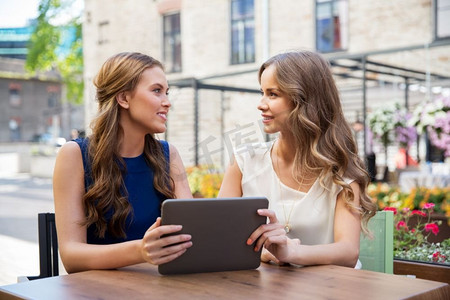 科技、生活方式和人的概念-快乐的年轻女性在户外咖啡馆里使用平板电脑。在户外咖啡馆玩平板电脑的快乐年轻女性