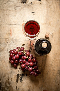 一串红葡萄配一瓶葡萄酒。在木制背景上。一串红葡萄配一瓶葡萄酒。