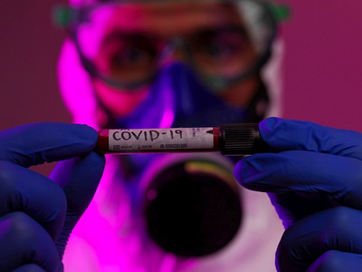 蓝色新冠摄影照片_冠状病毒，医生拿着阳性新冠病毒血样管。佩戴生物危害流行病防护口罩、防护服、发光。