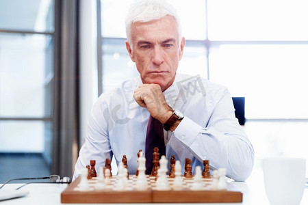 行动思考摄影照片_办公室里的生意人在下棋。思考下一步行动