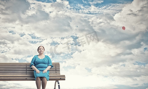 肥胖女性摄影照片_超重问题。一名身着蓝色连衣裙的中年肥胖女子坐在长凳上
