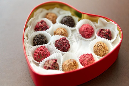 红心框摄影照片_糖果，糖果和食物概念—糖果在红色心脏形状的巧克力盒在棕色背景糖果在红心形状巧克力盒