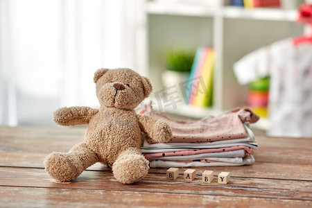 婴儿时代和服装概念—婴儿衣服，泰迪熊和玩具块在木桌子在家里。婴儿衣服和泰迪熊玩具在桌子上在家里