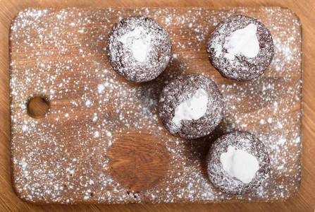 巧克力木板摄影照片_巧克力松饼，上面有白色的糖霜，放在撒有糖粉的木板上