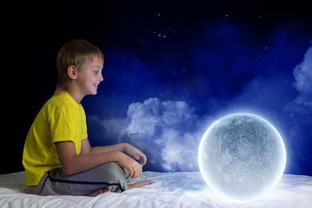 夜里做梦。可爱的男孩和月球星球坐在床上