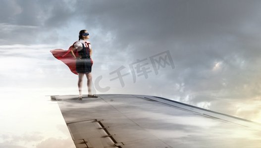 我是一个超级女孩。强大的超级英雄孩子女孩站在飞行飞机的翼