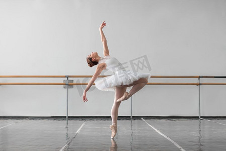 美丽的芭蕾舞女演员在芭蕾舞课上保持架子，背景是横梁和白墙。女芭蕾舞演员在课堂上保持紧张状态