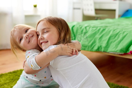 童年，家庭，表情和人的概念-快乐的小女孩或姐妹在家里拥抱。快乐的小女孩或姐妹们在家中拥抱