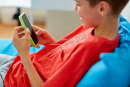 童年、科技与沟通理念--快乐微笑的男孩在家中拿着智能手机的特写。家里有智能手机的快乐微笑男孩