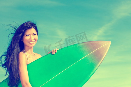 美丽的夏威夷年轻亚裔女子冲浪女孩，穿着比基尼，带着冲浪板，站在蓝天的海滩上