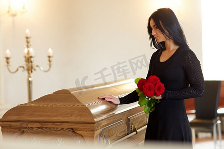 埋葬、人和哀悼的概念--教堂葬礼上戴着红玫瑰和棺材的不幸女人。葬礼上戴着红玫瑰和棺材的悲伤女人