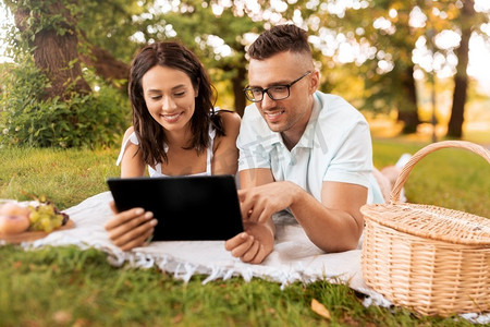 与人连接摄影照片_休闲与人概念—快乐夫妇与平板电脑电脑在夏季公园野餐。愉快的夫妇与平板电脑在野餐在公园