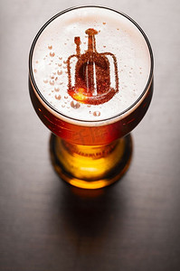 阅兵剪影摄影照片_本地精酿啤酒。啤酒厂的剪影在酒吧桌子上的一杯新鲜啤酒中，从高处俯瞰。本地精酿啤酒
