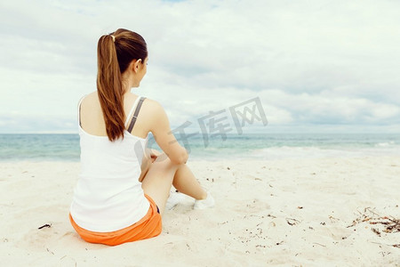 一位穿着运动服的年轻女子坐在海滩上。穿着运动服的年轻女子独自坐在海滩上休息一分钟