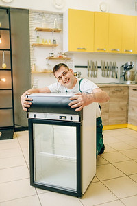 家杂摄影照片_身着制服的工人在家中拥抱冰箱。冰箱维修职业，专业服务