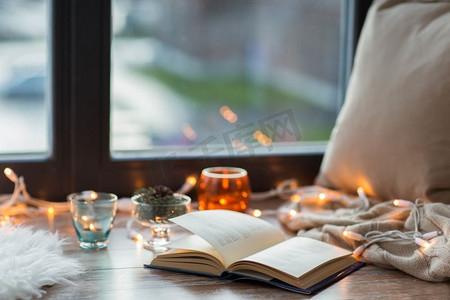 温馨舒适的家居概念书，窗台上的花环灯和蜡烛。书本、花环和窗台上的蜡烛