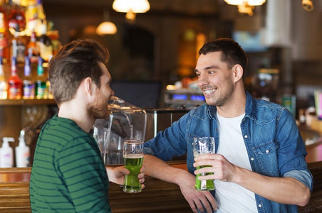 人，休闲和圣帕特里克节的概念-快乐的男性朋友在酒吧或酒吧喝绿啤酒。在酒吧或酒吧喝绿啤酒的男性朋友