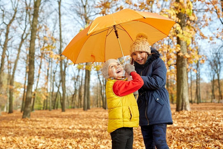 下雨打伞摄影照片_童年、季节和家庭概念-秋天公园里打伞的快乐孩子。秋天公园里打伞的快乐小朋友