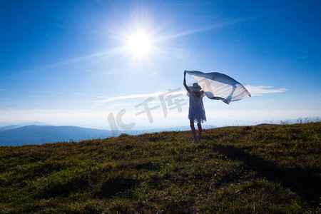 阳光与希望摄影照片_一位拿着纸巾的年轻女孩站在山顶享受阳光。女孩与自然的统一