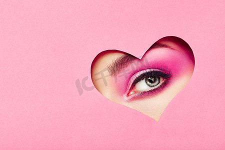 情人节和S的概念性照片。带着节日粉色妆容的女孩之眼。粉色背景上的纸心形。情人节是爱情的象征