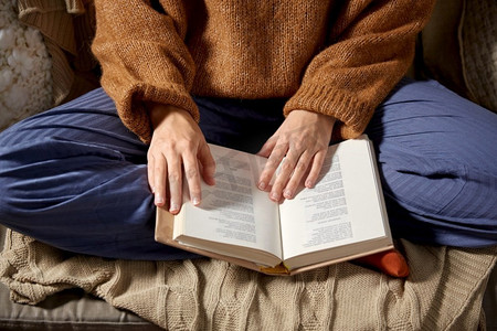 人，季节和休闲概念—近摄妇女在温暖毛衣阅读书在家里。妇女在温暖的毛衣阅读书在家里