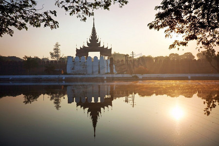 日出时，位于缅甸曼德勒的曼德勒宫殿周围的运河中倒影的古代棕色砖宫墙。