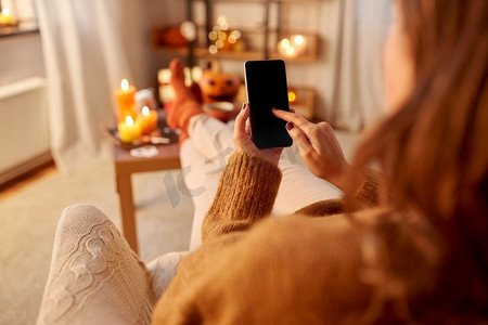 万圣节，假日和休闲概念—年轻妇女使用智能手机在家里。妇女使用智能手机在家里万圣节