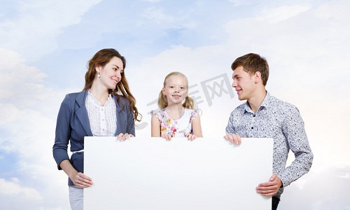 年轻的家庭。幸福的一家三口举着白色的空白横幅。文本位置