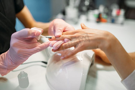 美甲大师在粉红色手套应用指甲油给女性客户，美容院。美甲师做指甲护理美容程序