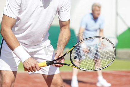男子的中段站着网球拍反对朋友打双打比赛在球场上