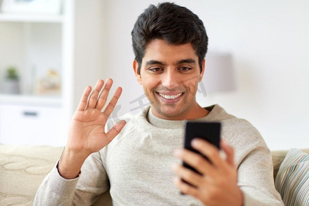 技术、人与沟通理念--智能手机在家视频通话的快乐男士。开心的男人在家里用智能手机进行视频通话