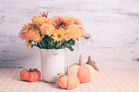 桌上摆着鲜花和橙色纺织小南瓜的花瓶。餐桌上的秋日装饰