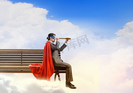 超级英雄坐在板凳上，看着望远镜。穿着超级英雄服装的家伙