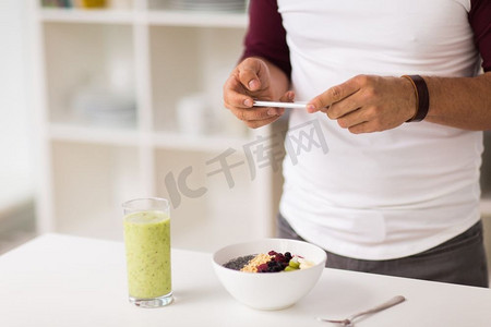 吃早饭摄影照片_健康饮食，科技和人的概念-在家中厨房吃早餐的智能手机人。带着智能手机的男人在家吃早饭