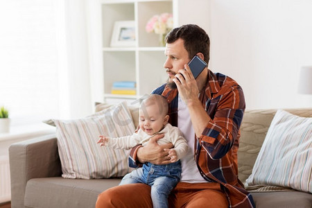 家庭、父母和人的概念--带着小男孩的父亲在家里用智能手机打电话。父亲带着孩子在家里用智能手机打电话