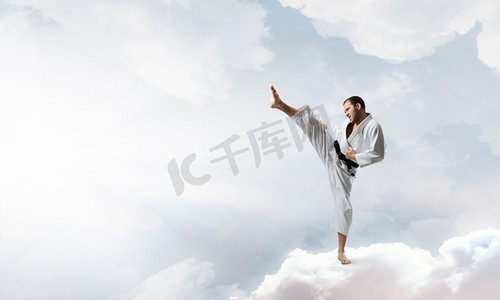 穿着白色基米诺的空手道男。年轻坚定的空手道人在高空中的云上
