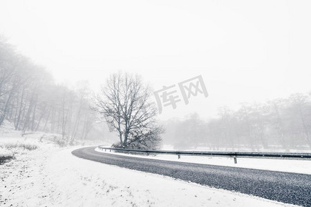 雾蒙蒙的冬日风景中弯弯曲曲的高速公路，路边有棵树和雪