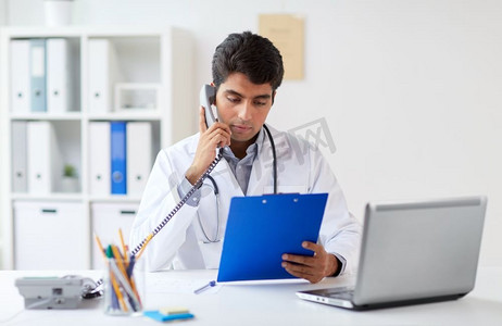 医学、保健和人的概念--男医生拿着剪贴板在诊所打电话。拿着剪贴板的医生在诊所打电话
