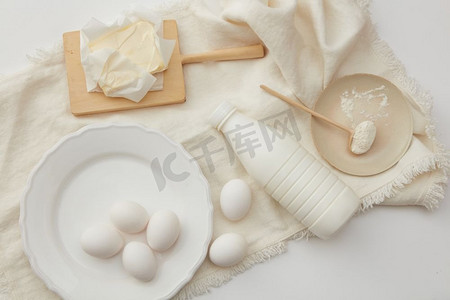 平铺摄影照片_鸡蛋、牛奶、面粉和黄油在白色餐巾上烘烤蛋糕，平铺。烘焙蛋糕配料