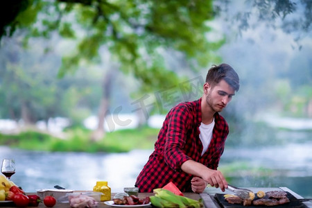 鸡架摄影照片_烹饪在烧烤烤架的美味食物的人为户外法国晚餐聚会在美丽的夏天晚上在自然界