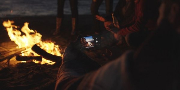 男孩在海滩篝火旁给女孩看手机上的一张照片