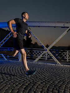 城市体育，年轻健康的男子慢跑过桥的城市在清晨在夜间