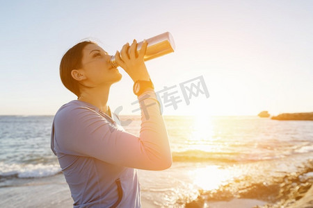 女人在海滩上喝水。年轻女子饮用水后行使在海滩上