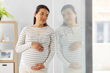 怀孕、休息、人与期待的概念--怀孕的亚洲妇女在家中抚摸自己的肚子。怀孕的亚洲妇女在家中