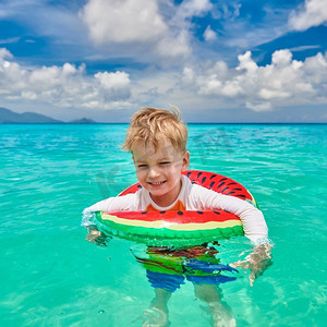 游泳管摄影照片_塞舌尔海滩上三岁蹒跚学步的男孩戴着充气环游泳