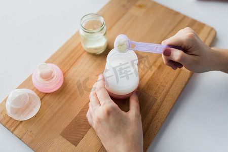 食物和营养概念-母亲的手与婴儿奶瓶和勺子准备婴儿配方奶粉。手拿奶瓶和勺子制作配方奶