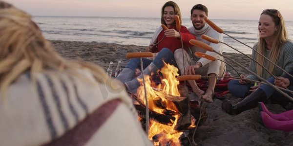 一群年轻的朋友深夜坐在火堆旁，烤着香肠，喝着啤酒，聊天，玩得很开心