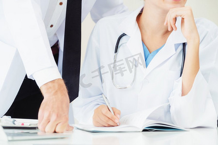 医院办公室的医生在与站在她旁边的另一位医生交谈时，在病人报告上写笔记。