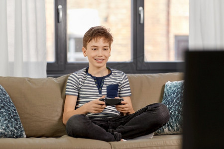 休闲，科技和儿童概念-微笑的男孩，带着游戏手柄在家玩电子游戏。戴着游戏手柄在家玩电子游戏的男孩