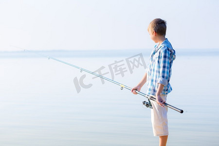 穿蓝衬衫的男孩站在馅饼上。穿着蓝色衬衫的男孩站在海边的码头上，手里拿着一根钓鱼竿